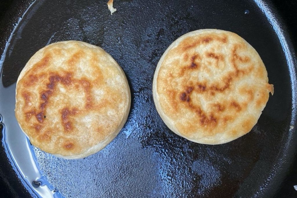 Sourdough crumpets frying on the second side.