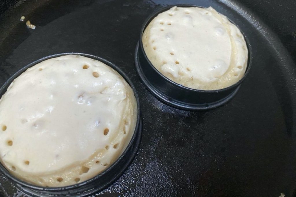 Crumpets in ring molds on a skillet.